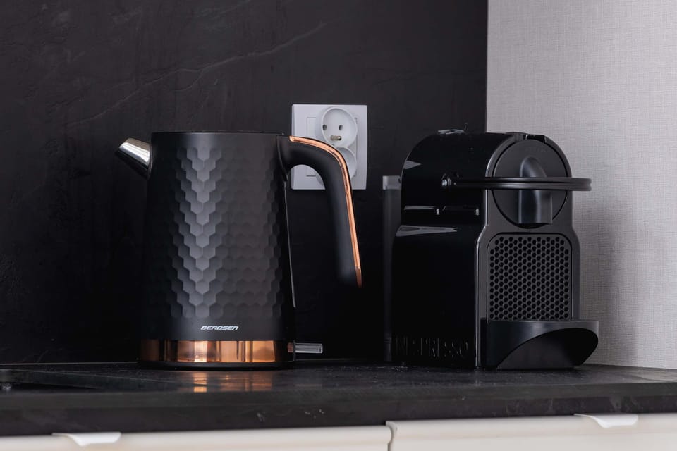 There is a black kettle and a coffee machine on the kitchen counter.
