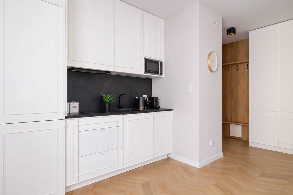The functional kitchenette with white furniture and a black wall between the decor matches the rest of the room.