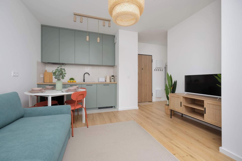 The modern living room and kitchen area featuring a teal sofa, light pendant, and open-concept layout.