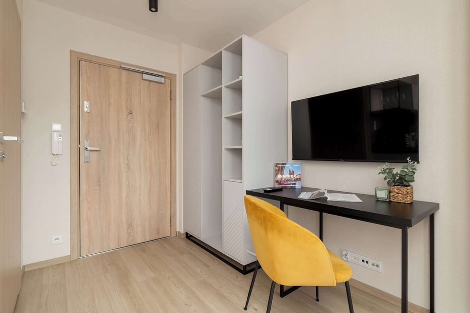 A multi-functional living area with a comfortable sofa, a wall-mounted TV, and a desk with a yellow chair for work or study.