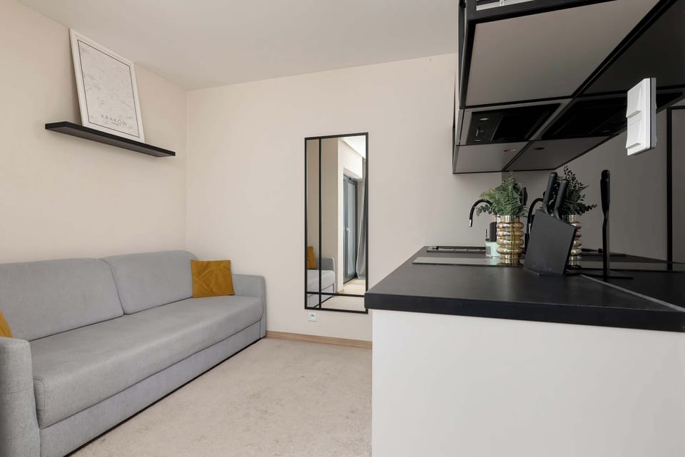 A bright living space with a modern gray sofa, yellow accent pillows, a minimalist shelf, and a large mirror.