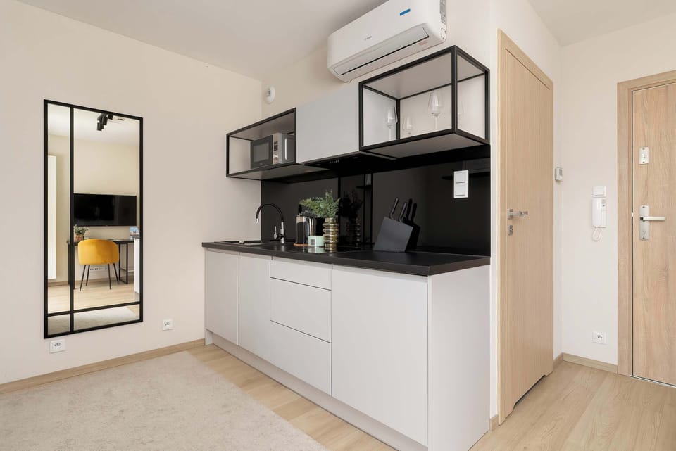 A compact and functional kitchenette with white cabinets, black countertops, and a small dining table by the window.