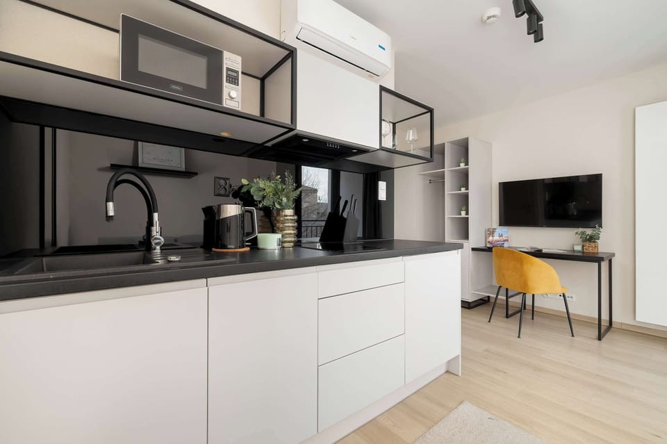 A compact and functional kitchenette with white cabinets, black countertops, and a small dining table by the window.