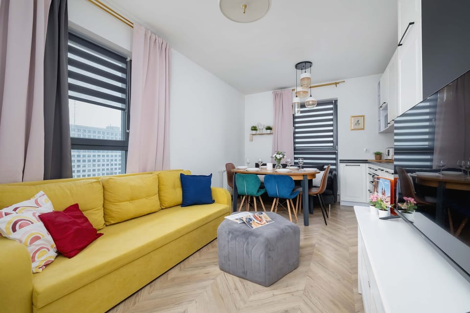 A living room with a TV on the wall, bright furniture and a yellow sofa.