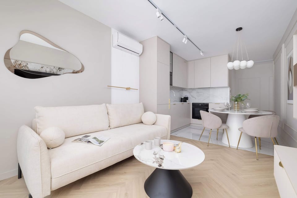 A seating area with a small cream loveseat, wall-mounted mirror, and soft lighting that creates a warm and intimate ambiance.

