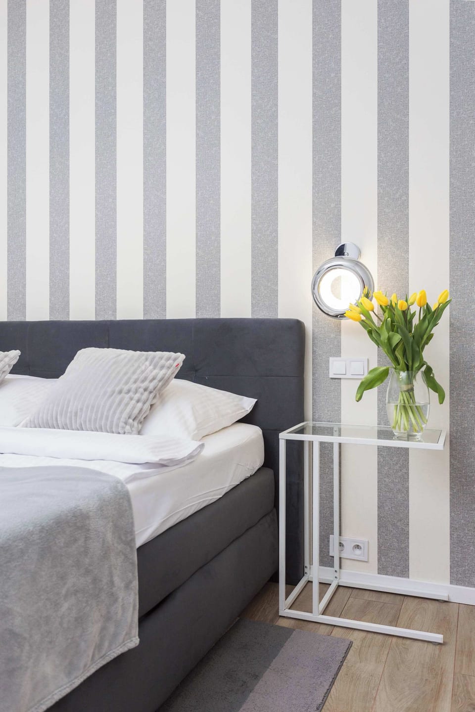Another angle of the bedroom, highlighting the plush bedding and the bedside table with a decorative flower vase. The lighting creates a warm atmosphere.