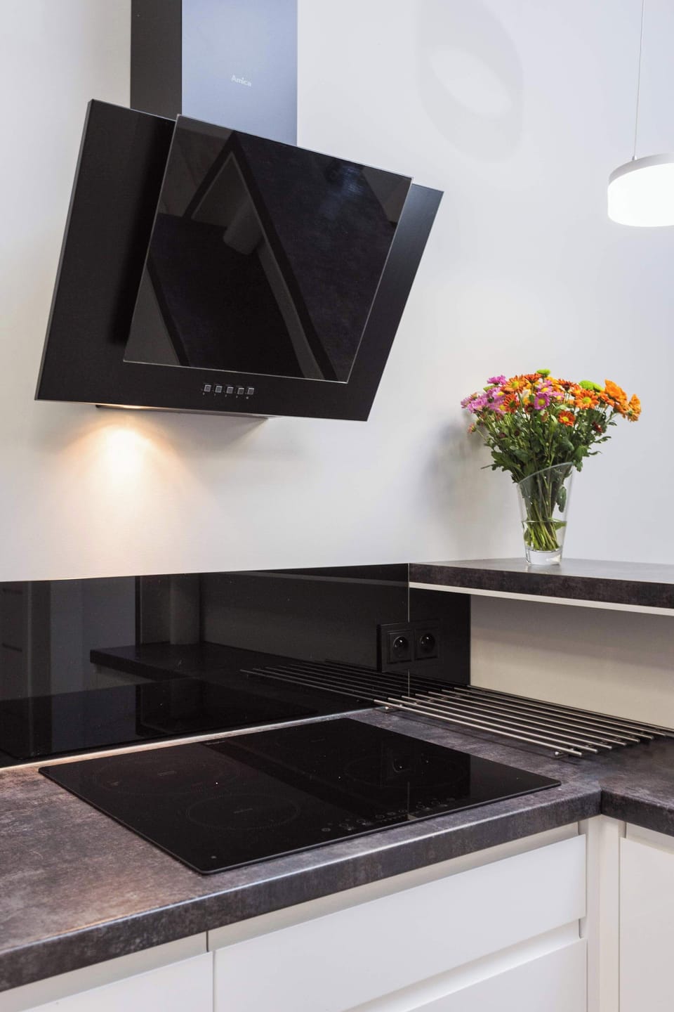 A close-up of a black kitchen sink with a modern faucet, placed against a dark backsplash. A small potted plant adds a fresh touch.