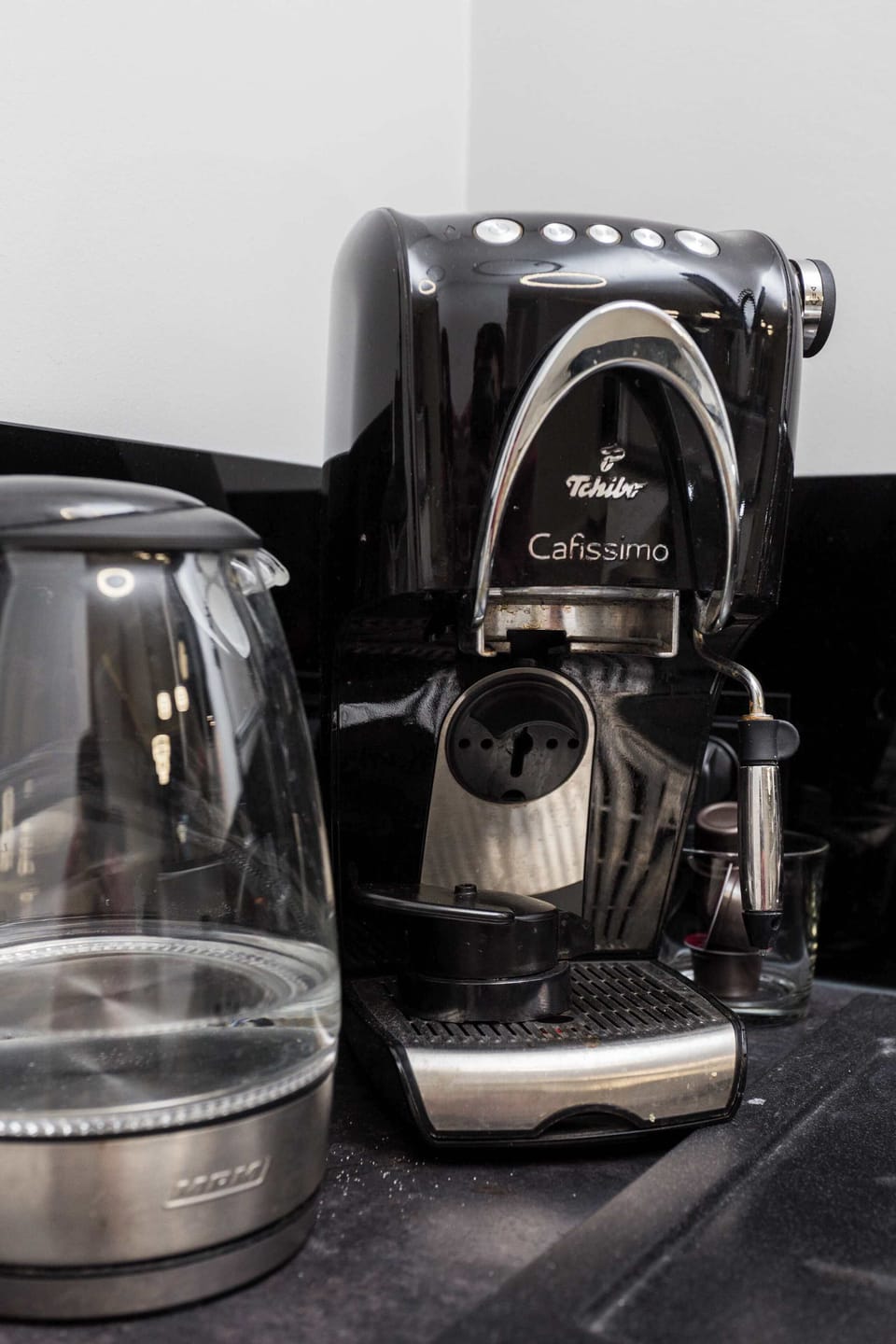 A close-up of a black coffee machine with a glass kettle placed next to it. The glossy surfaces reflect light elegantly.