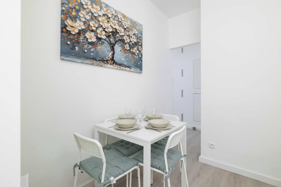 A small table set for two beneath a floral painting creates a cozy spot for a romantic dinner.

