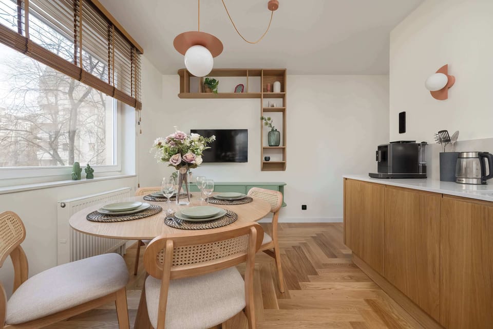 Dining area with round table, TV under which is a green cabinet. To the right of the table is the kitchenette.