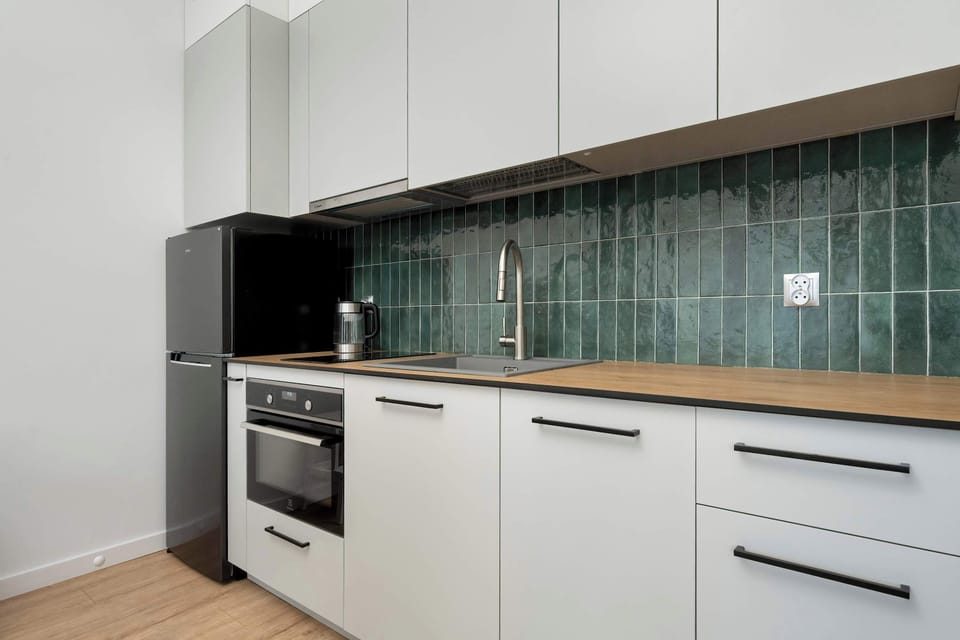 A modern kitchen with white cabinets, a green tile backsplash, and built-in appliances.