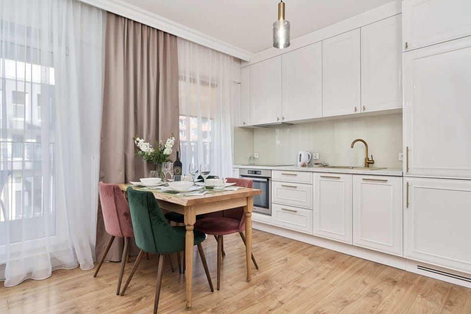A compact kitchen featuring white cabinets, a dining table with chairs, and a modern, open-plan design.