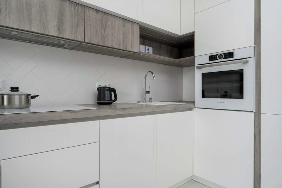 A minimalist kitchen with upper wooden cabinets and lower white ones, equipped with a kettle and built-in oven.