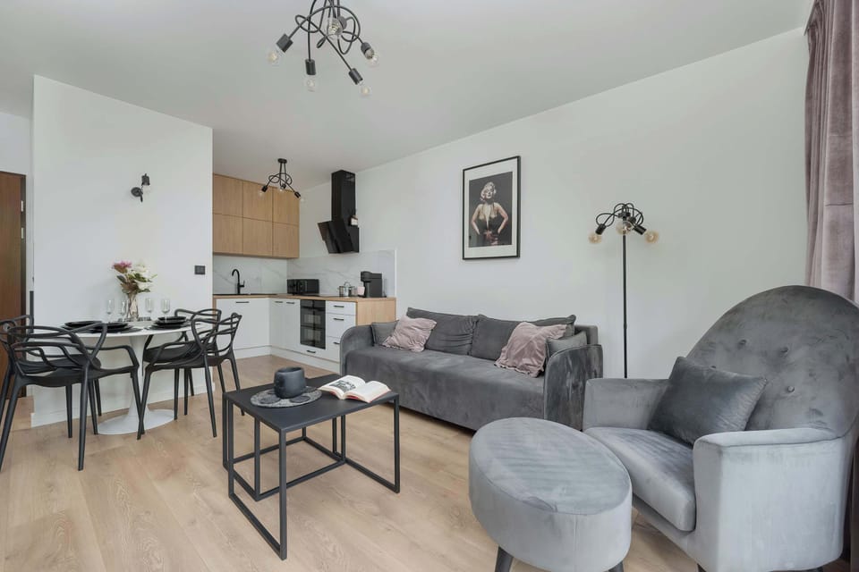 A compact living room with a TV, L-shaped couch, and open kitchen design, blending black and natural wood tones.