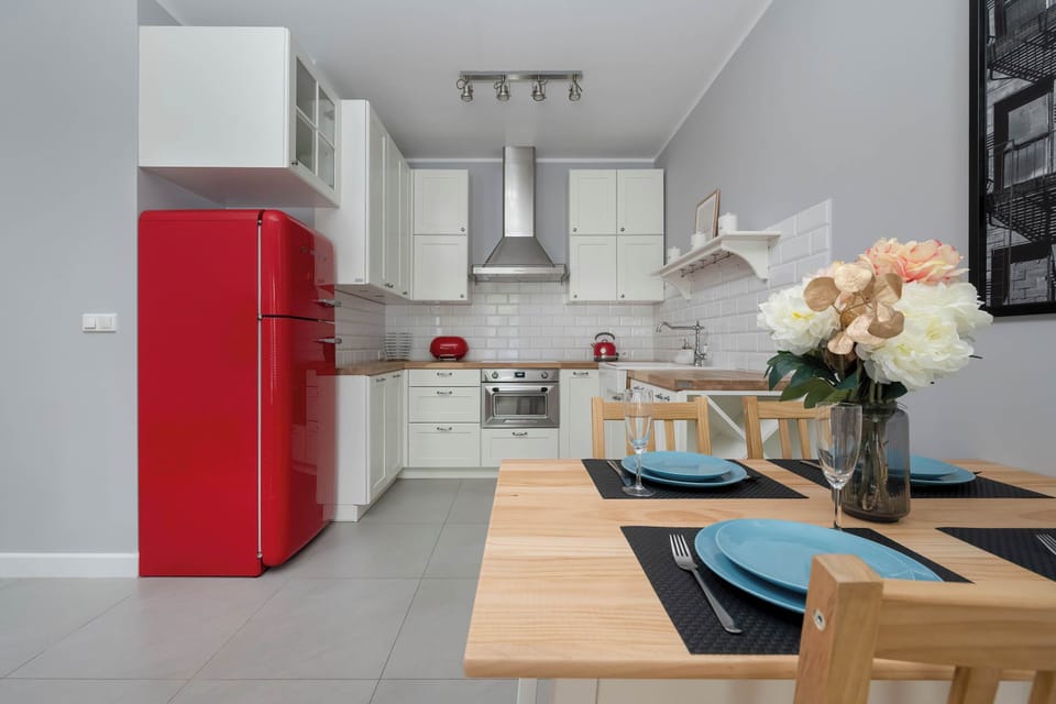 A modern kitchen with white cabinets, silver handles, and red accents like a kettle and fridge blends functionality with aesthetics.