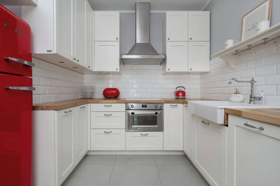 A modern kitchen with white cabinets, silver handles, and red accents like a kettle and fridge blends functionality with aesthetics.