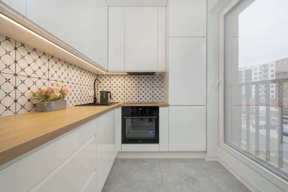 Bright and clean kitchen design with white cabinets, wood countertops, and a patterned backsplash. Appliances are sleek and built-in.