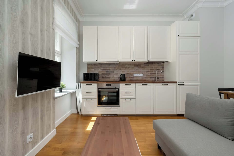 A full kitchen with white cabinetry, modern appliances, a small dining nook, and a mounted TV, blending cooking and lounging spaces.