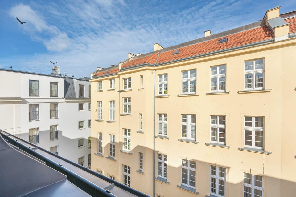 A view from the window of a historic building across the street, with warm yellow walls and red rooftops visible.