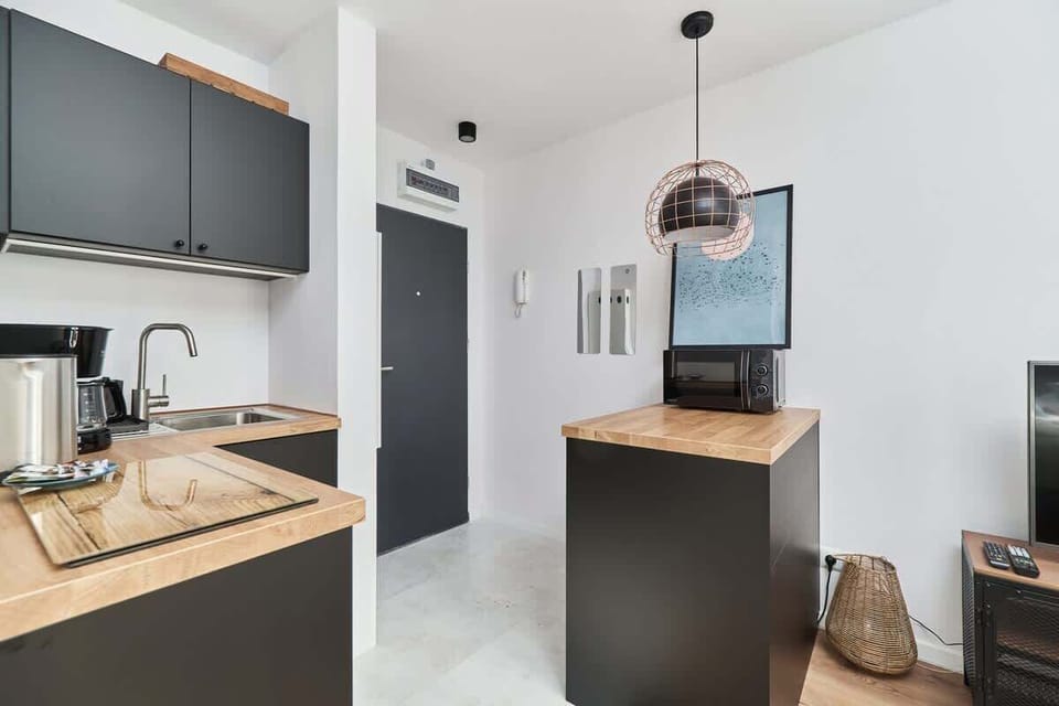A modern kitchenette with sleek black cabinets, a wooden countertop, and appliances, including a coffee maker and kettle.