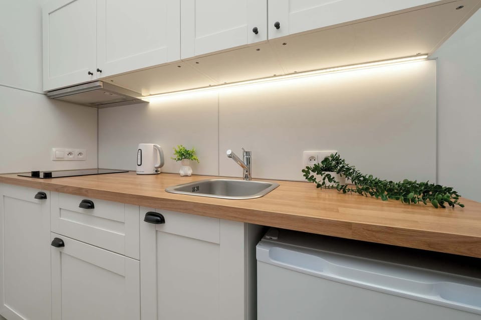 View of the kitchenette with a focus on the white cabinets, sink and built-in stove. It’s a sleek, modern kitchenette with a minimalist design.