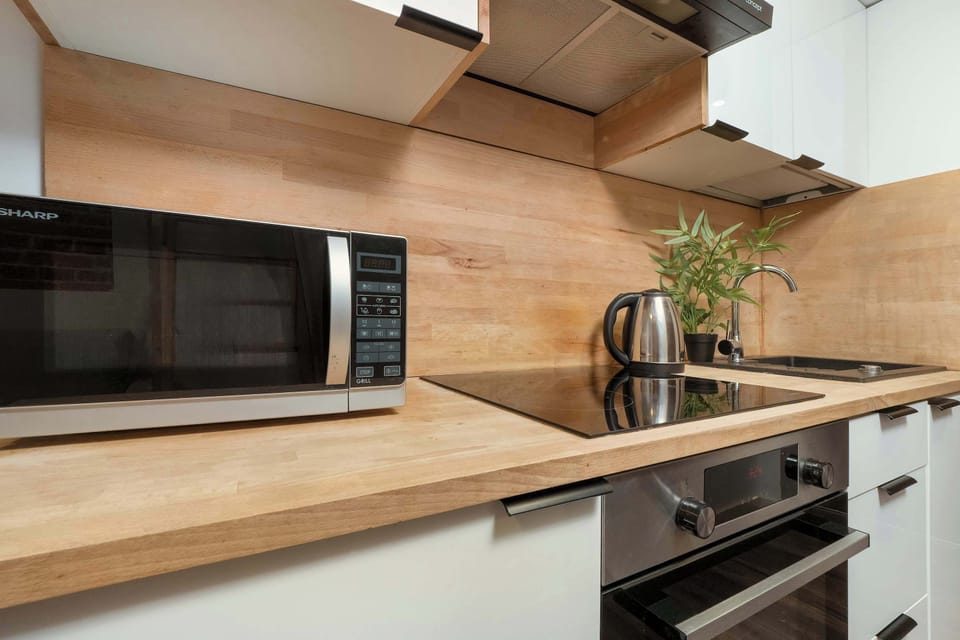 A kitchenette featuring a wooden countertop, a microwave, and an electric stovetop, surrounded by modern white cabinets.