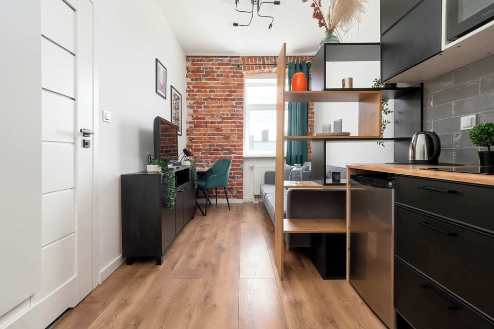 A wide view showing the hallway opening into the living area and kitchenette with wooden flooring and modern decor.