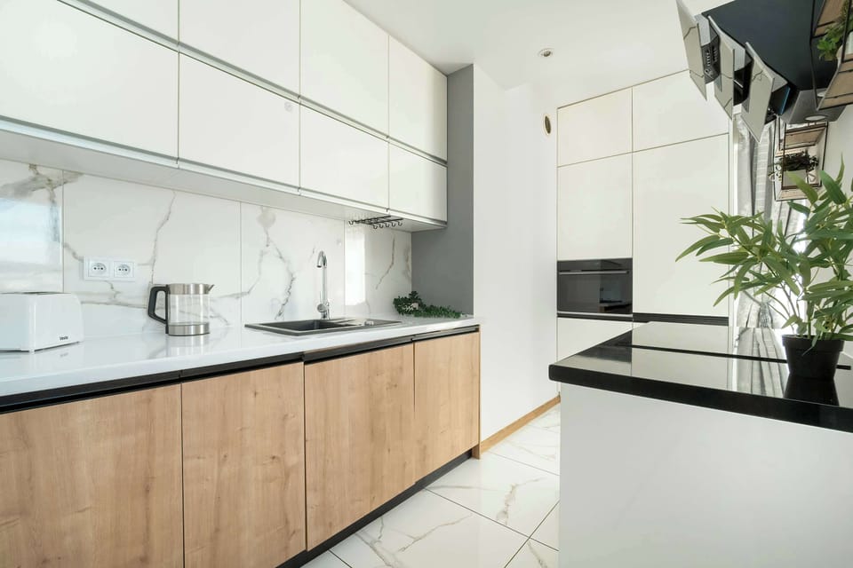 A modern kitchen with white and wooden cabinetry, black countertops, and stainless-steel appliances, providing a sleek look.