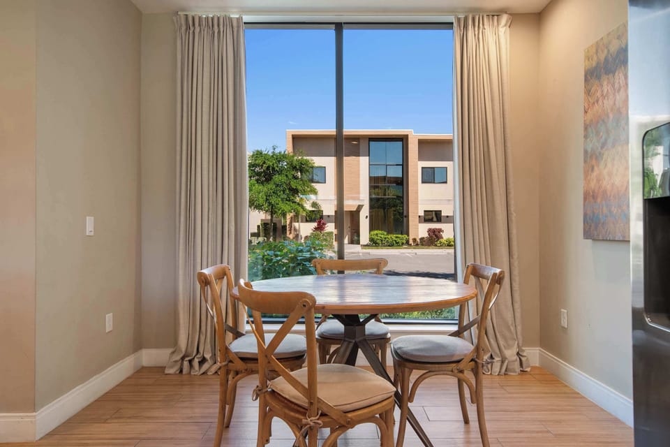 Bright dining nook with large window, natural light, and charming wooden chairs.
