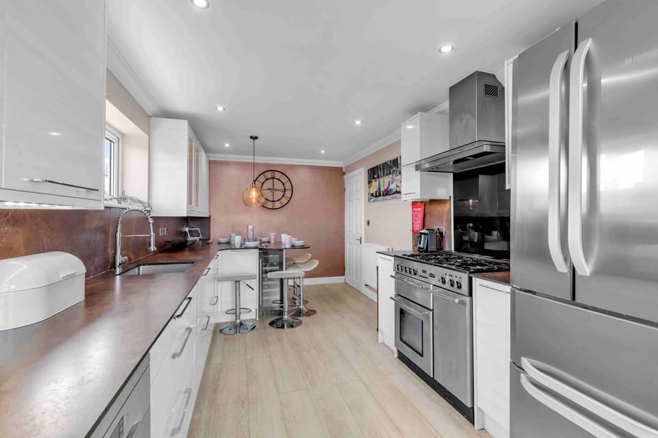 Sleek kitchen featuring electric hob, oven, microwave, fridge-freezer, dishwasher, and washer-dryer with bright cabinetry and tiled splashback