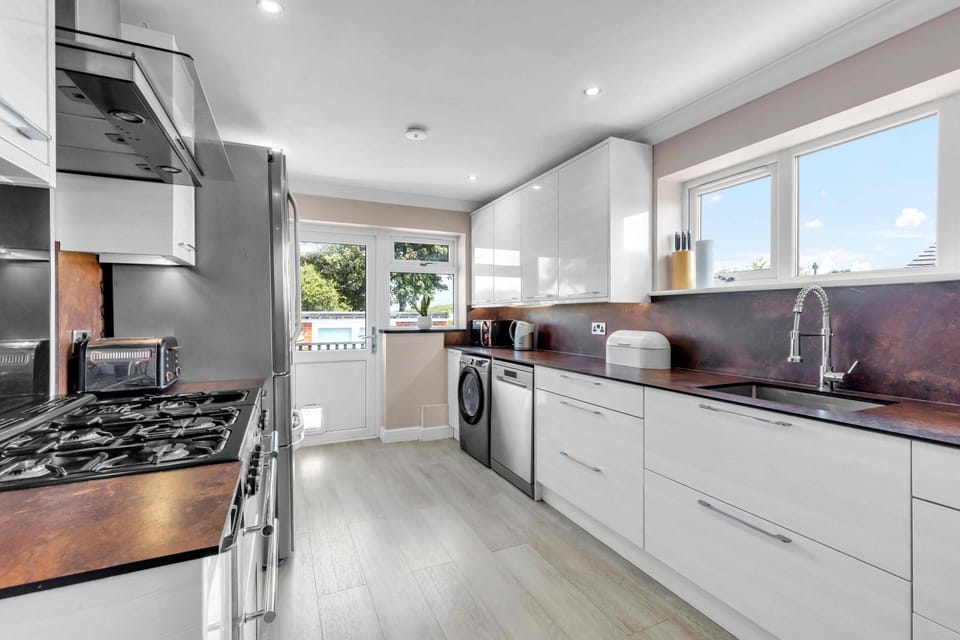 Sleek kitchen featuring electric hob, oven, microwave, fridge-freezer, dishwasher, and washer-dryer with bright cabinetry and tiled splashback