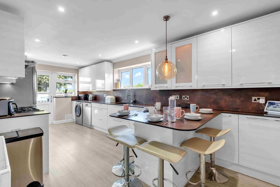 Sleek kitchen featuring electric hob, oven, microwave, fridge-freezer, dishwasher, and washer-dryer with bright cabinetry and tiled splashback