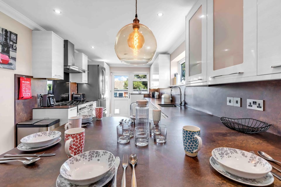 Sleek kitchen featuring electric hob, oven, microwave, fridge-freezer, dishwasher, and washer-dryer with bright cabinetry and tiled splashback