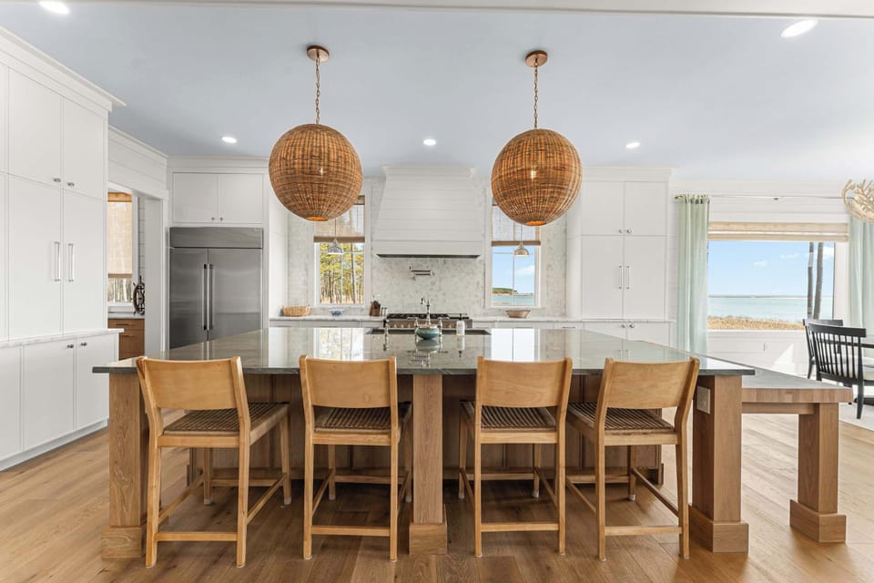 Anchored by a dramatic island with seating for four, this chef’s kitchen combines artisanal textures with sleek modern finishes. Statement woven pendants add warmth above the gleaming stone countertop too.