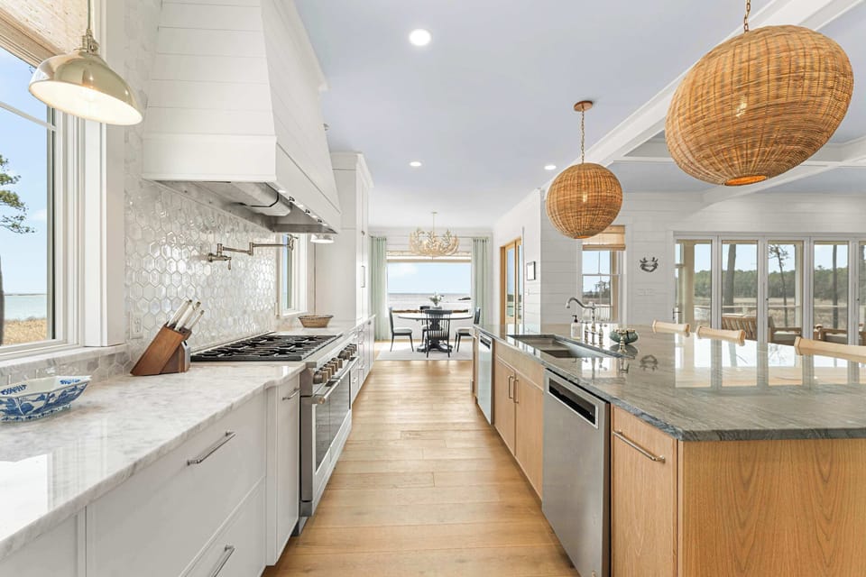 This stunning kitchen aisle stretches between culinary craftsmanship and visual serenity. Prep meals at the sleek dual-basin island or admire the glistening bay just steps beyond the dining nook. Here, thoughtful luxury meets practical elegance.
