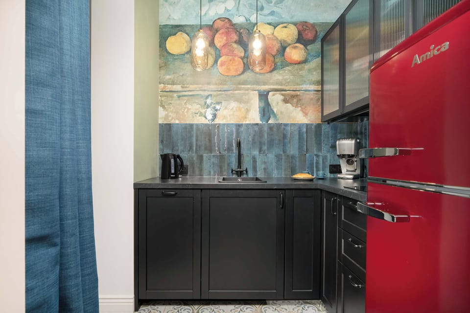 A wide view of the fully equipped kitchen, including a red fridge, black cabinetry, and a colorful mural that ties the space together.

