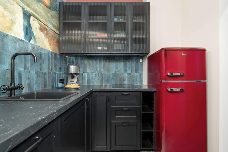 A stylish kitchen with black cabinetry, a vivid red retro refrigerator, and a deep blue tiled backsplash under open shelves.