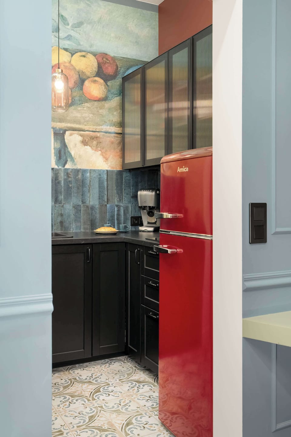 A partial view of the red fridge and kitchen entrance with patterned flooring, adding contrast and vintage charm to the apartment.