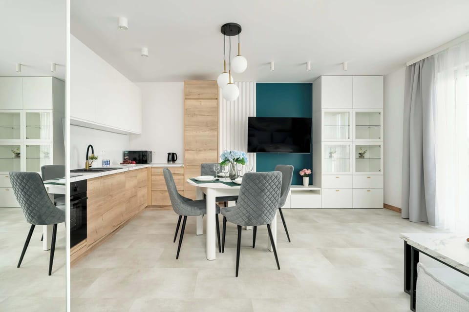 A dining area with a dark gray table and matching chairs, a teal accent wall, and a view into the kitchen.