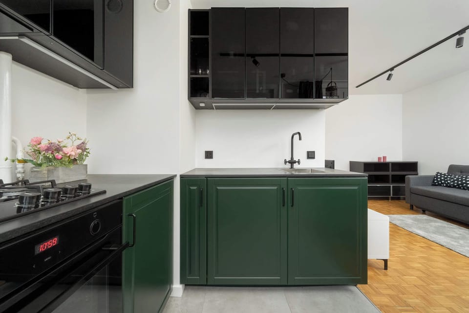 Modern dark green kitchenette with such appliances as a kettle, a gas stove, and a washing machine.