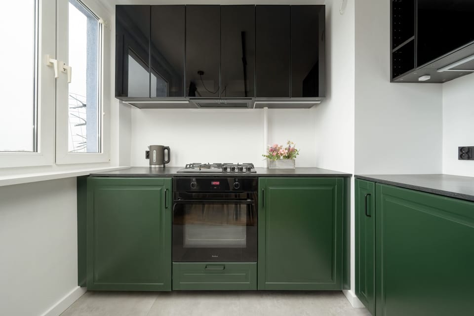 Elegant dark green kitchenette with such appliances as an oven, a microwave, and a fridge.