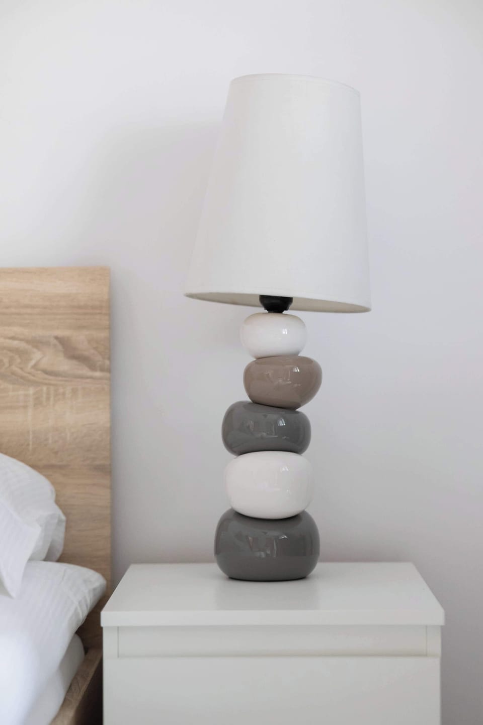 A close-up of a white nightstand with a modern lamp placed on top, next to the bed.