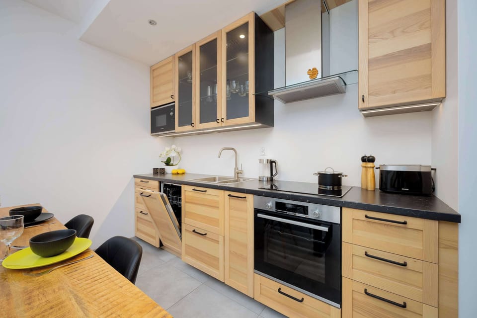 A close-up of the kitchen counter with a modern black backsplash and neatly arranged items like a cutting board and plants.