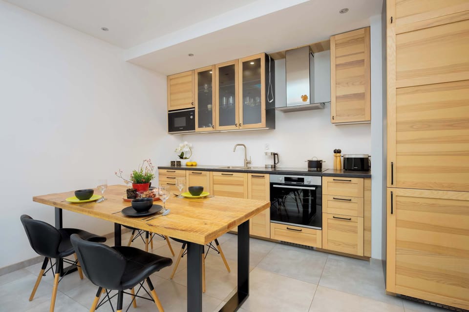 A combined kitchen and dining space with light wood cabinets, a dining table, and chairs. The kitchen is fully equipped with modern appliances.