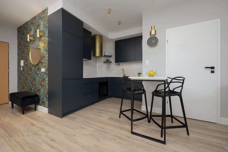 A sleek and contemporary kitchen with dark cabinetry, brass accents, and bar stools. The space is fully equipped for cooking and dining in comfort.