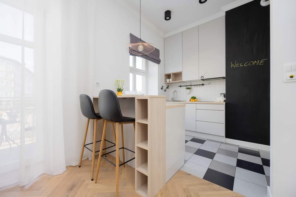 Welcome to this chic and functional studio, featuring a stylish kitchen bar perfect for enjoying meals, a modern kitchenette, and a welcoming chalkboard, all bathed in natural light from a nearby window.