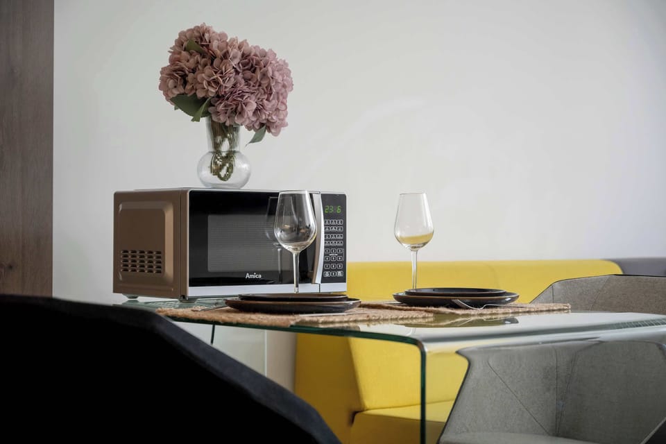 Imagine enjoying a delightful meal at this elegantly set glass table, complemented by a modern microwave for your convenience and a beautiful floral centerpiece adding a touch of charm.