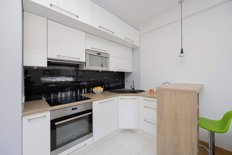 A well-equipped kitchenette with white cabinets, a built-in oven, and a black backsplash.
