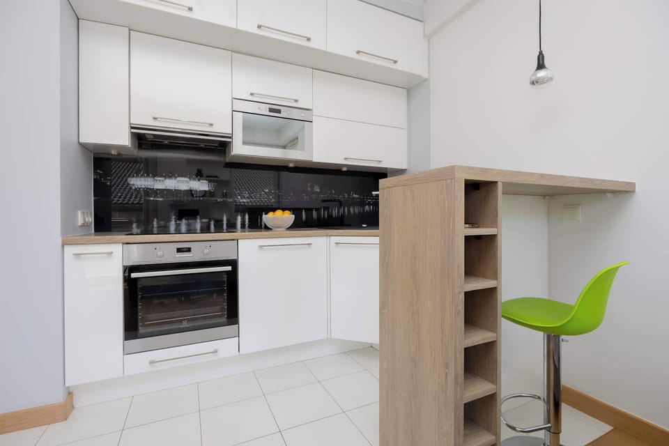 A well-equipped kitchenette with white cabinets, a built-in oven, and a black backsplash.