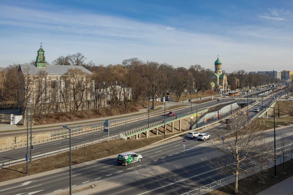 A busy thoroughfare with greenery and historic buildings in the background visible from the window.